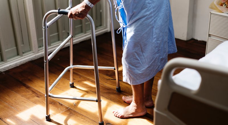 Senior using a walking frame with warm sunlight on hardwood floors