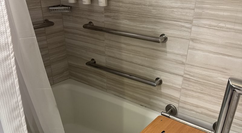 Bathroom with stainless steel grab bars and fold-down shower seat installed for safety